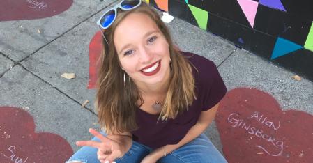 Costs & Services au pair sitting on the pavement, smiling into the camera